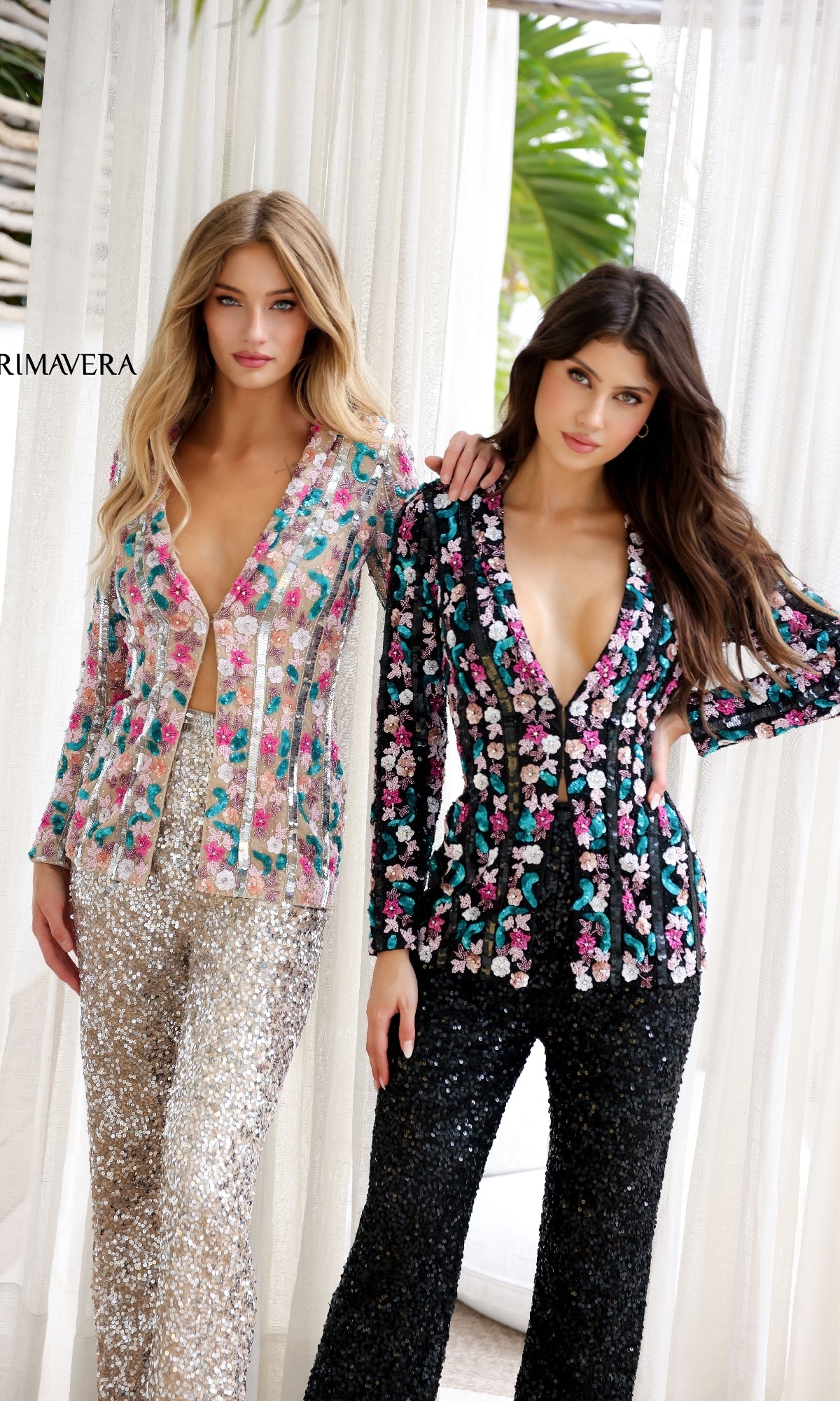 Two women stand side by side in the Primavera 4388 Long Sequin Formal Jumpsuit—one in silver and pastel, the other in black multicolor—with sheer white curtains as a backdrop.
